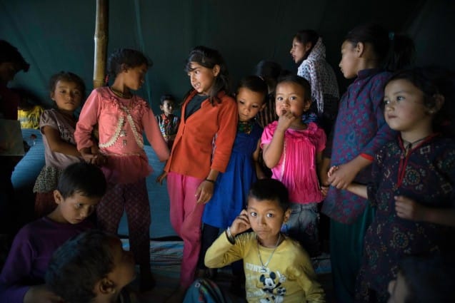 Jamuna Nepali, 9, (center, red) and other children attend a UNICEF-supported Child Friendly Space in the camp for earthquake-displaced people where they are staying on a wind-swept ridge above the town of Charikot, Dolakha District, Nepal on May 25 2015. On 25 April a magnitude 7.8 earthquake killed more than 8,000 people and destroyed massive amounts of property, including numerous temples that were on the list of UNESCO World Heritage Sites. A major aftershock measuring 7.3 with an epicenter in Nepal's Dolakha District followed on 12 May 2015 with dire consequences to human life, livestock and property. UNICEF and its partner organizations are distributing shelter, hygiene and nutritional supplies across quake-affected areas of Nepal. Nepal Earthquake - Back to School Package - Photos from Dolakha - Day 2