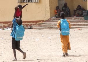 On 18 March 2015, a boy lifts a younger child high in the air in play, in a camp for people displaced by the Boko Haram conflict, in Yola, capital of the north-eastern state of Adamawa, which has been affected by the escalating Boko Haram insurgency. Another boy walks nearby. The two older children, who are on their way to school, carry backpacks that bear the UNICEF logo. In March 2015 in Nigeria, 15.5 million people, including 7.3 million children, are affected by the continuing crisis in the countrys north-eastern region. More than 1.2 million Nigerians have fled their homes as a result of violence and attacks by Boko Haram insurgents that have escalated since the beginning of 2015. Many of the displaced, most of whom are children and women, are sheltering with in host communities that have limited resources, and in formal and informal camps. All are in urgent need basic supplies, health and nutrition services, and critical water sanitation and hygiene support to prevent the spread of disease. Over 150,000 people, the vast majority children and women  have also fled to neighbouring Cameroon, Chad and Niger, further straining vulnerable communities  some of which are already facing food insecurity and malnutrition, are prone to disease outbreaks and natural disasters, and often already host hundreds of thousands of refugees, returnees and migrants who have escaped violence and hardship throughout the region. The impact of the crisis on children and women is of particular concern. Many of them have lost their homes and belongings escaping with only the clothing they were wearing; and some have walked for days  or even weeks  to find refuge. Many children in the region have been traumatized and are in need of psychosocial support. They have witnessed violence and atrocities, including seeing parents and siblings slaughtered by Boko Haram insurgents; and have been exposed to or have experienced violence and brutality. Their homes have been bur